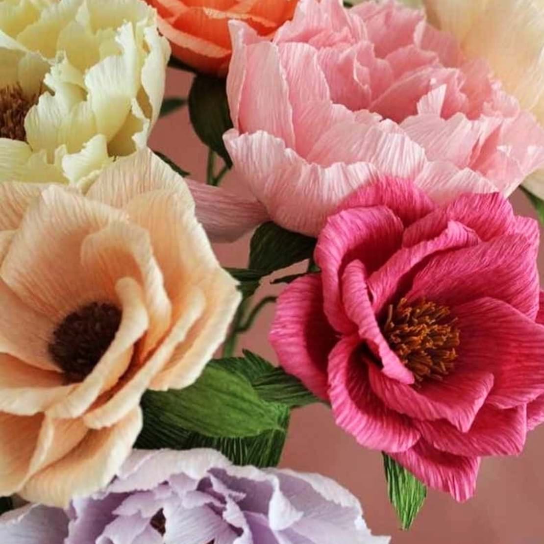Blomster i farverne rød, orange og rosa. Blomsterne er udført i crepe papir.